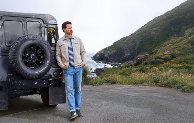 Mann lehnt an Jeep vor Küstenlandschaft