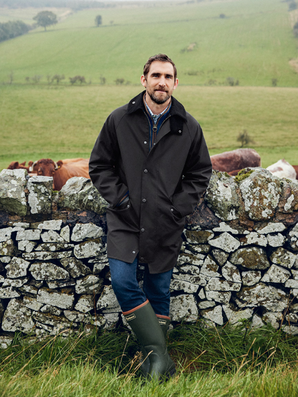 Mann in Barbour-Jacke vor Mauer