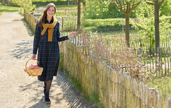 Frau am Gartenzaun im Flanellkleid mit OBstkorb