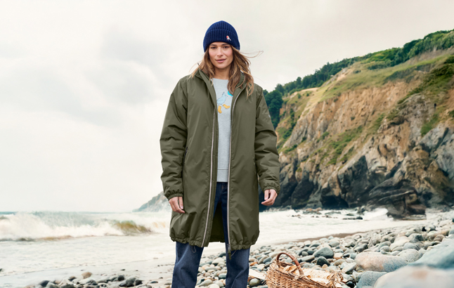 Frau im Parka mit Müllmütze und Motivshirt am Strand