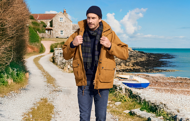Mann in gelber Outdoorjacke an einem Küstenweg