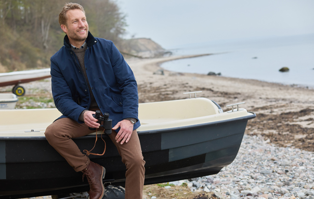 Mann sitzt auf Rand eines Ruderboots am Ufer