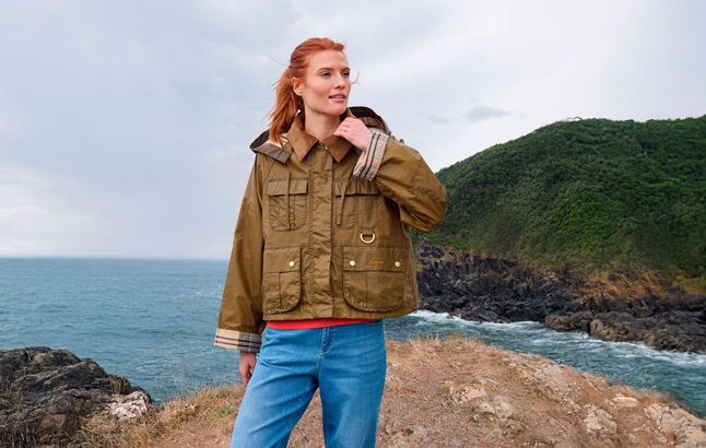 Frau in kurzer Barbour-Jacke vor Küste