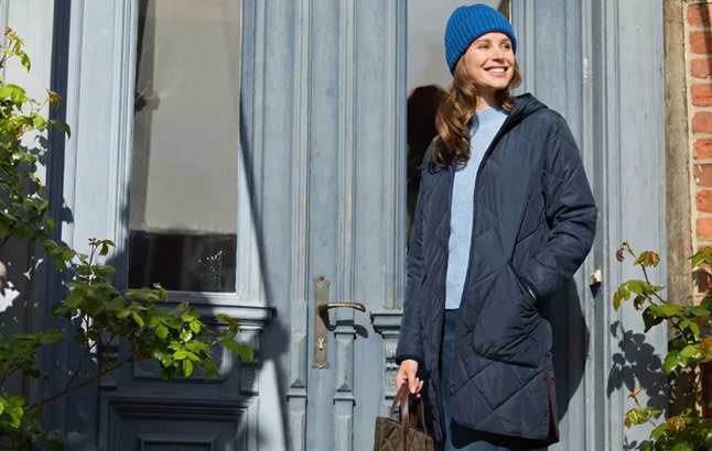 Frau trägt Steppmantel mit Pullover und Strickmütze in Blau