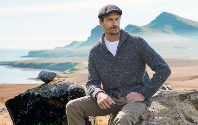 Mann sitzt auf Fels, Berg und Meer im Hintergrund